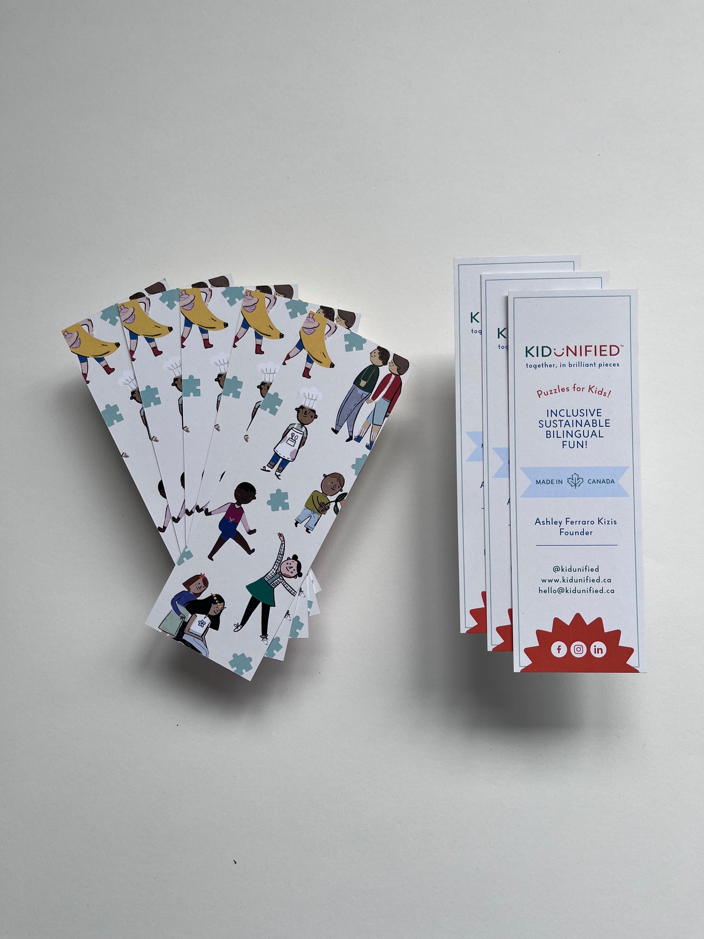 Six bookmarks waved out in a fan on a white background. The bookmarks have illustrations of children of various ethnicities, cultures, disabilities and gender expressions. Three books marks with contact information are in a row beside the fan.
