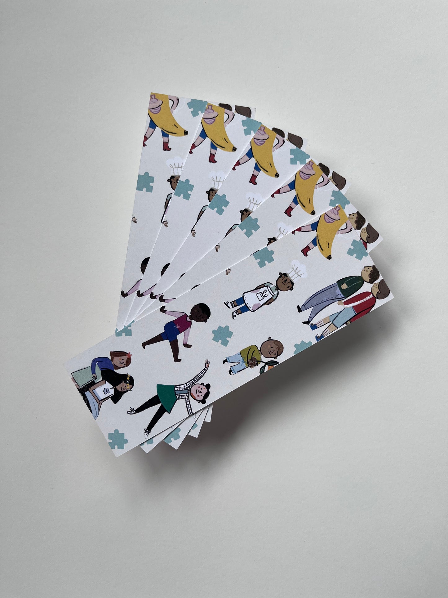 Six bookmarks waved out in a fan on a white background. The bookmarks have illustrations of children of various ethnicities, cultures, disabilities and gender expressions.